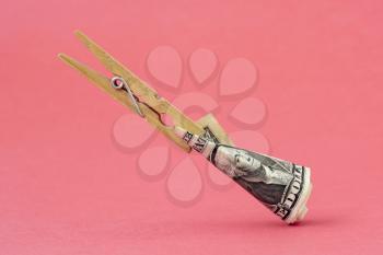 Wooden clothespin with one dollar floating over pink background