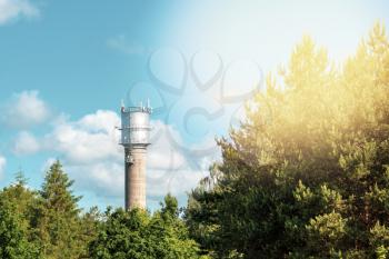 Water tower with communication antennas over a green tree tops with sunlight