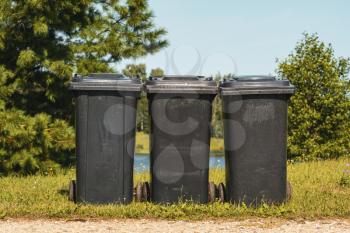 Three black plastic waste bins in the city park