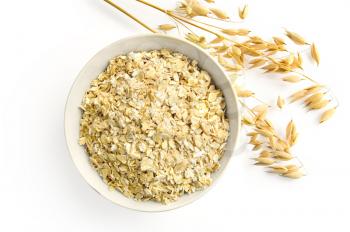 Rolled oats in a bowl with ripe stalks of oats is isolated on a white background