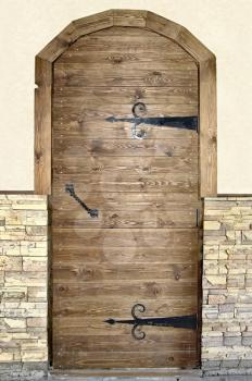 Brown wooden door with black metal handles and hinges on a beige background of whitewashed walls and decorative wooden