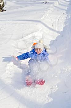 Little girl sliding down a hill in the snow in winter