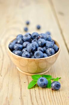 Blueberries in a wooden bowl with a sprig of green leaves on the background of wooden boards