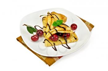 Two pancakes with berries cherries, mint, chocolate icing on a white plate and napkin isolated on white background