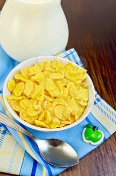 Yellow corn flakes with milk in a jug, spoon, napkin against a wooden board