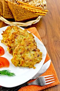 Fritters of minced chicken on a white plate with tomato and fennel, knife, fork, orange napkin, a basket of bread and crispbreads on a wooden board