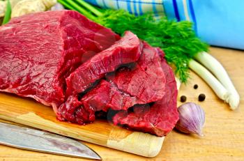 A piece of beef, garlic, pepper pots, dill, green onions, ginger root, blue napkin, a knife on a wooden board