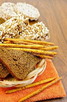 Fresh rye bread, bread sticks, and various crispbreads in a wicker tray and the orange napkin against a wooden board