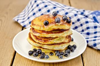 A stack of pancakes with blueberries and honey on a white plate, napkin against a wooden board