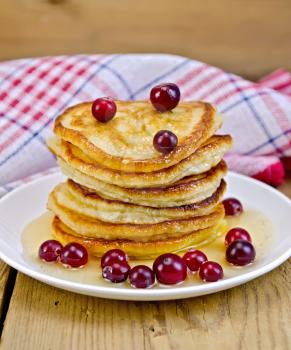 A stack of pancakes with cranberries and honey on a white plate on a wooden boards background