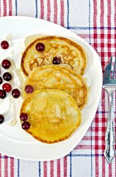 Pancakes with cranberries and honey on a white plate, fork on napkin background
