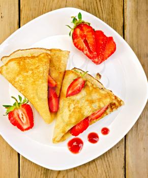 Two pancakes with strawberries and jam on a white plate on a wooden boards background