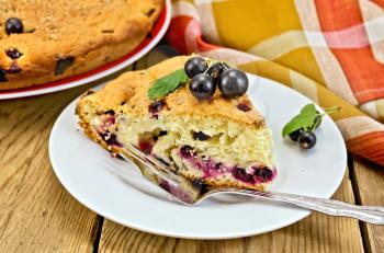 Sweet piece of cake with black currant and fork on a plate, napkin on the background of wooden board