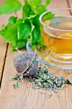 Metal sieve with dry mint leaves, herbal tea in a glass cup, fresh mint leaves on the background of wooden boards