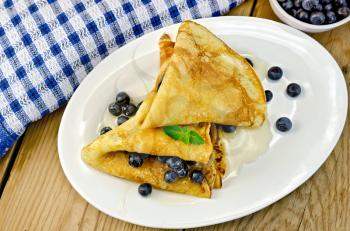 Two pancakes with blueberries, mint and honey on a white plate, napkin, cup on the background of wooden boards
