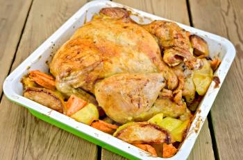 Chicken baked with potatoes, carrots and apples in a tray on the background of wooden boards