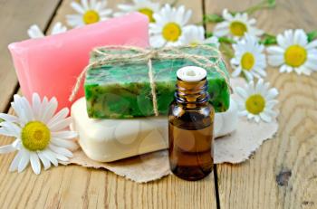 Oil in a bottle, different soaps on a piece of paper, daisy flowers on a background of wooden boards
