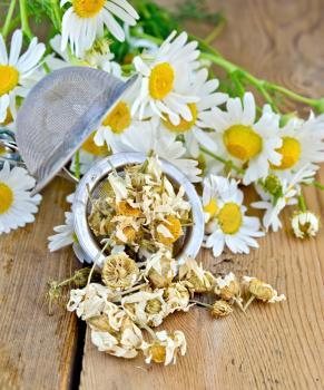 Metal sieve with dried chamomile flowers, fresh flowers daisies on a background of wooden boards