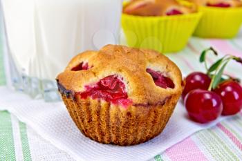 Cupcakes with cherries on a paper napkin, cherry, milk in a glass on a background of a linen tablecloth