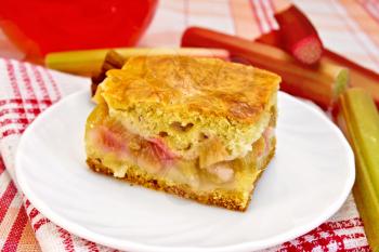 A piece of sweet cake with rhubarb, rhubarb stalks, cinnamon, pitcher compote on linen tablecloth background