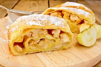 Strudel with apples, apples, tea strainer on the background of wooden boards