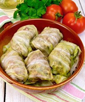 Stuffed cabbage meat in cabbage leaves in a ceramic pan on a napkin, tomatoes, parsley on a lighter background board