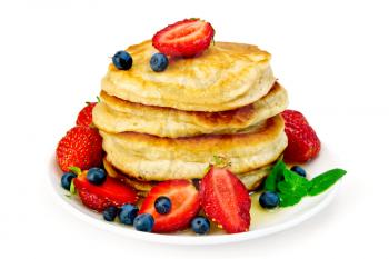 A stack of pancakes with strawberries, blueberries, mint and honey on a white plate isolated on white background