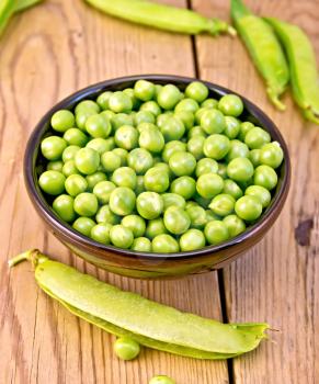 Green peas in a brown bowl, pea pods on the background of wooden boards