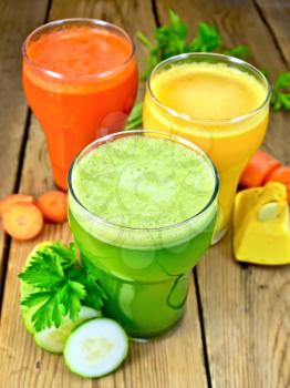 Three tall glassfuls with juice of carrot, cucumber and pumpkin, vegetables on wooden board