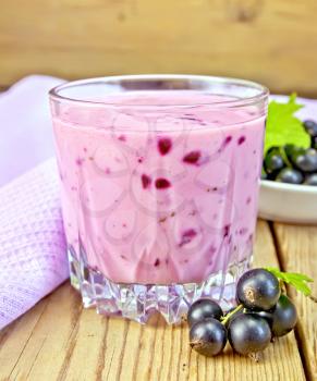 Milkshake with black currants in a glass, purple cloth, a saucer with berries currants on a wooden boards background