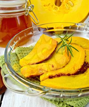 Pumpkin baked with honey in a glass pan on a napkin, a jar of honey, raw pumpkin on a lighter background of wooden boards