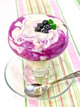 Dessert milk with blueberry, cornflakes, curd, spoon in a glassware on a background of a linen tablecloth
