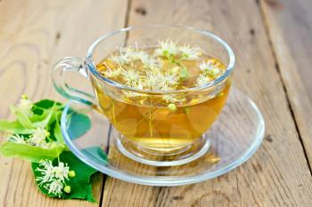 Herbal tea in a glass cup, fresh linden flowers on a wooden boards background