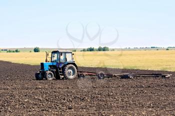 Blue wheeled tractor on the background of plowed land, cereals and sky