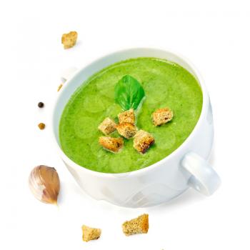 Green soup puree in a white bowl with crackers, spinach, garlic, pepper isolated on white background