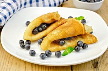 Two pancakes with blueberries and mint on a white plate, napkin, bowl on a wooden boards background