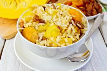 Pilaf fruit with pumpkin, raisins, dried apricots in a bowl on a saucer, pumpkin, dried fruit, napkin, spoon on a background of light wooden boards