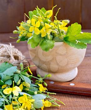 A bunch of flowers celandine in a wooden mortar and on the table, ball of twine, knife on background wooden planks