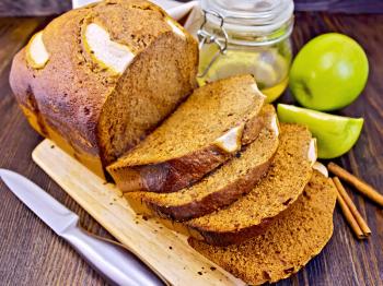 Canadian apple bread with honey and cinnamon, green apple, napkin and a knife on a dark wooden board