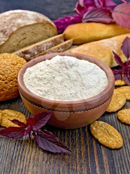 Amaranth flour in a clay bowl, bread, biscuits, purple amaranth flower on the background of wooden boards