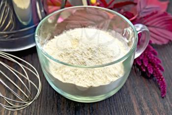 Amaranth flour in a glass cup with a mixer and a sieve, purple amaranth flower on the background of wooden boards