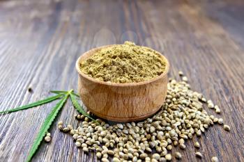 Hemp flour in a bowl, corn and green leaves of hemp on a background of wooden planks