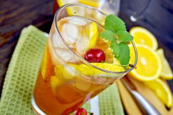 Lemonade in a glass with a cherry, lemon and orange, mint green napkin on board with fruit on the background of dark wooden board