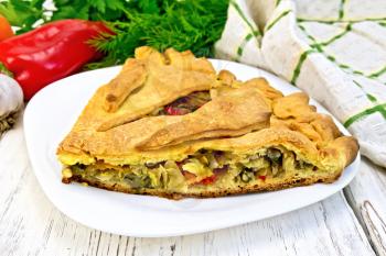 Pie with cabbage, sorrel and peppers on a plate, napkin, parsley on the background light wooden boards