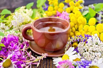 Herbal tea in a clay cup of fresh flowers fireweed, tansy, chamomile, clover, yarrow, meadowsweet, mint leaves on a dark wooden board