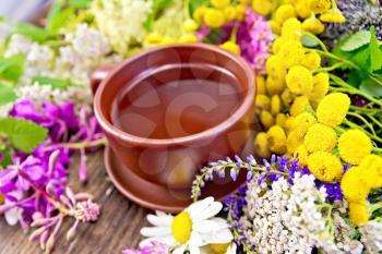 Herbal tea in a clay cup of fresh flowers fireweed, tansy, chamomile, clover, yarrow, meadowsweet, mint leaves on a wooden boards background