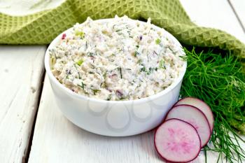 Pate of cottage cheese, dill and radish in a bowl, radish slices, dill and a napkin on a wooden boards background