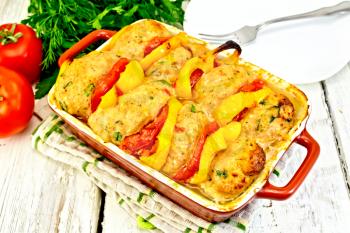 Cutlets of turkey meat baked with tomatoes and yellow pepper in a ceramic roasting pan on a kitchen towel, parsley on a wooden boards background