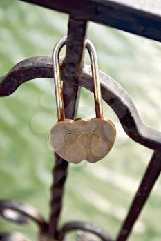 Bronze padlock in the form of two hearts on the iron fence on a background of water
