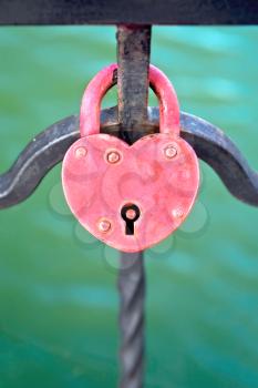 Red padlock in the shape of heart close up on a fence on a background of water